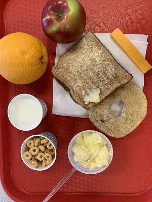 An image of slice of toast, bagel, apple, orange, slice of cheddar cheese, cup of milk, cup of yogurt and cup of Cheerios cereal.
